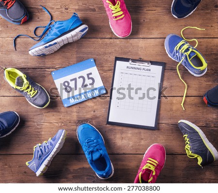 Various running shoes, race number and running plan laid on a wooden floor background