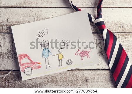 Fathers day composition with childs drawing and colorful tie laid on wooden desk backround.