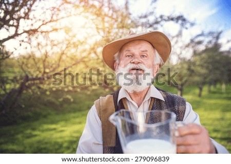 Senior farmer with milk in a glass jug outside in green nature