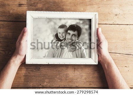 Man holding a picture frame with family photo on a wooden background.