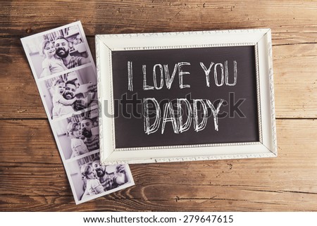 Picture frame with I love you daddy sign and instant photos on wooden background.