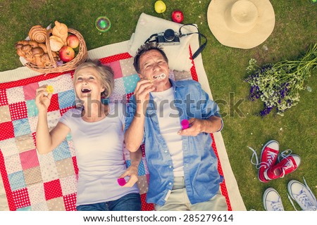 Beautiful seniors having a picnic in nature and blowing bubbles