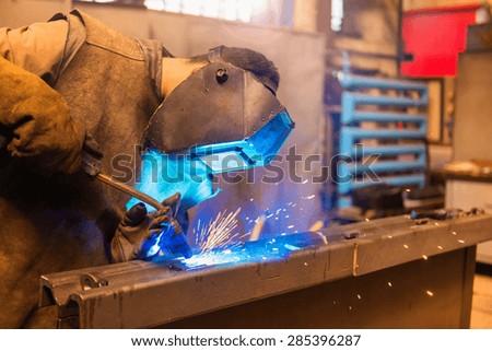 Young man with protective mask welding in a factory
