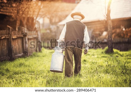 Senior farmer carrying kettle full of milk