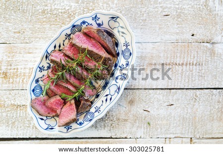 Grilled beef steak, sliced on a serving plate with fresh rosemary spring