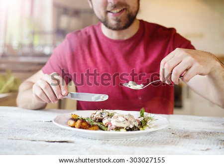 Unrecognizable man holding fork and knife cutting food on a plate