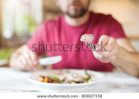 Unrecognizable man holding fork and knife cutting food on a plate