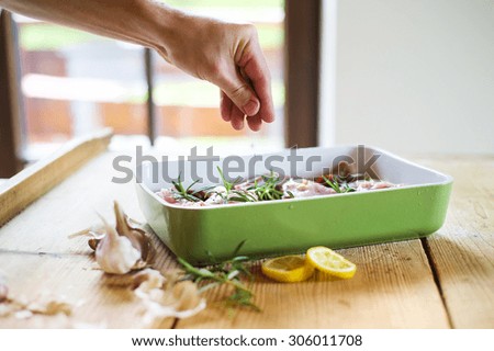 Raw fresh rabbit meat with salt, pepper, rosemary leaves and garlic, on a green tray ready to be cooked