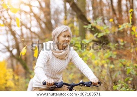 Active senior woman riding bike in autumn nature.