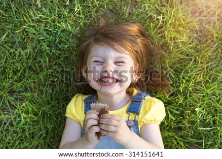 Cute little girl with chocolate face lying on a grass