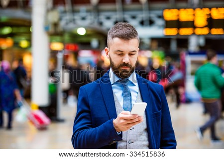 Young handsome businessman with smart phone standing at the crowded station