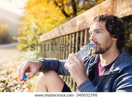 Young handsome runner with water bottle sitting on a bridge