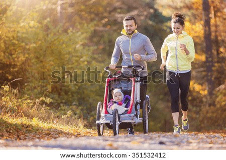 Beautiful young family with baby in jogging stroller running outside in autumn nature