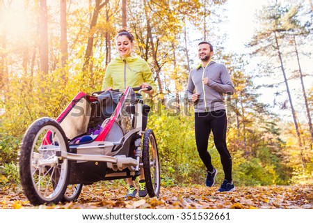 Beautiful young family with baby in jogging stroller running outside in autumn nature