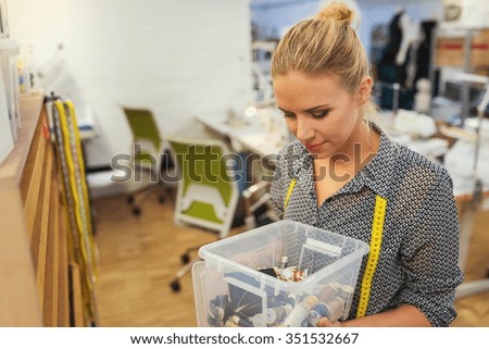 Beautiful young tailor woman holding a  box full of threads