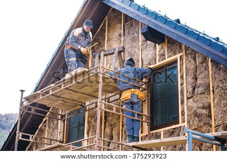 Construction workers thermally insulating house facade with glass wool.