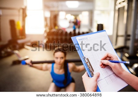 Woman exercising in gym, personal trainer, plan on clipboard