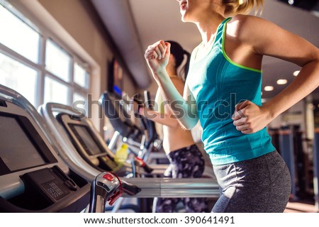 Two fit women running on treadmills in modern gym