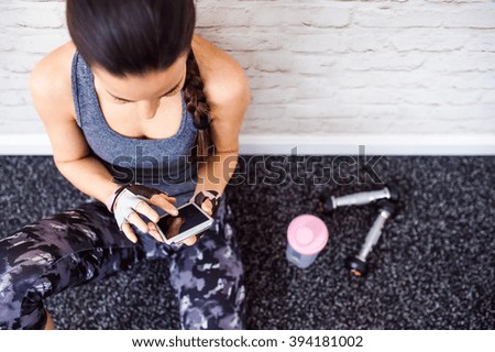 Fit woman in gym holding smart phone, brick wall