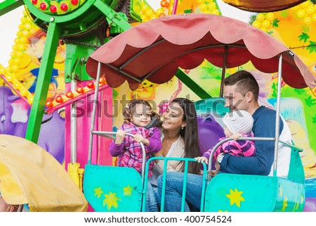 Father, mother, daughters enjoying fun fair ride, amusement park
