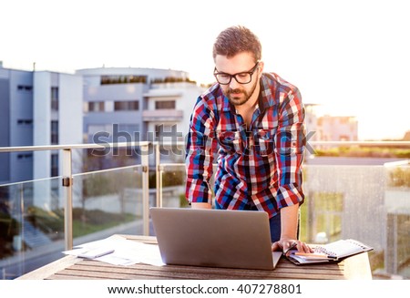 Businessman working from home on laptop, standing on balcony