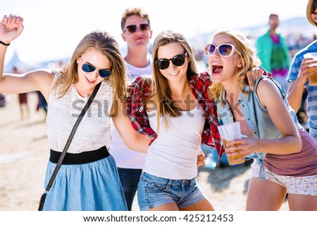 Group of teenagers at summer music festival, sunny day. Young teens at summer music festival. Funny group of young girls at music festival. Crazy teens with beer at summer festival.