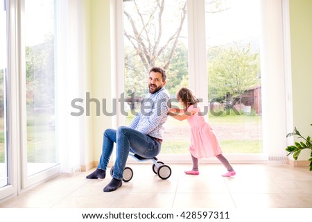 Father and daughter playing together, riding a bike indoors