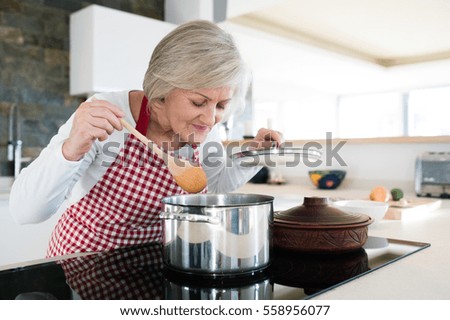 Senior woman in the kitchen cooking, mixing food in a pot.