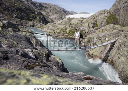 Man walking over a bridge over waterfall near Svelgabreen glacier (Folgefonna National Park, Hordaland county, Norway)