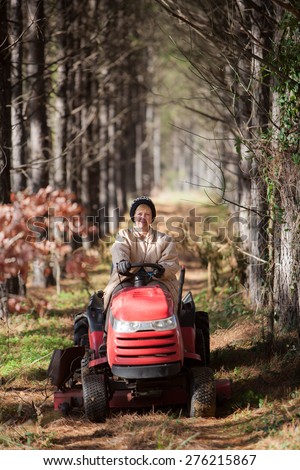 Senior woman driving a tractor through a grove of trees in Winter