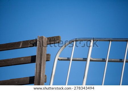 Wooden fence and metal gate juxtaposed against a bright blue sky.