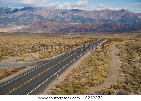 A lonely stretch of deserted desert highway with parallel dirt road, extended into the distance.  Highway 50, Nevada.