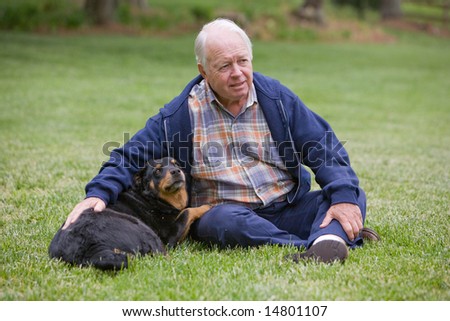 Retired gentleman sitting in the grass with his furry canine companion looking off into the distance.