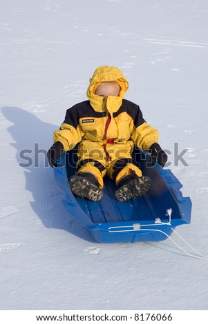 Young Bundled Up Boy Peeks Slightly Out of Hood While Riding in Sled