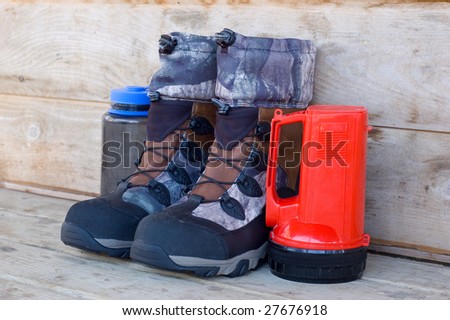 Boots, Water Bottle and Flashlight Against Wooden Cabin Wall