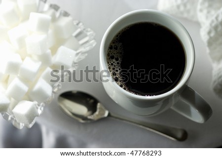 Black coffee in white cup with sugar cubes and spoon on white table cloth