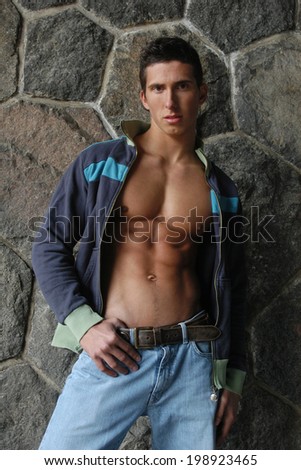 Young muscular man in an unzipped jacket in front of a stone wall.