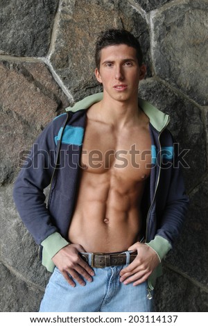 Young muscular man in an unzipped jacket in front of a stone wall.