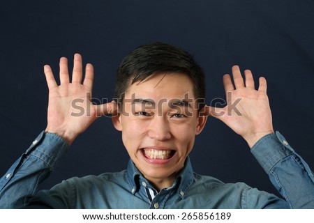 Funny young Asian man making face and looking at camera