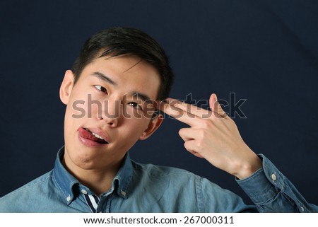 Funny young Asian man pointing fingers against his temple as suicide sign