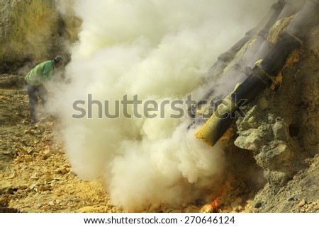 KAWAH IJEN, INDONESIA - AUGUST 8, 2011: Miner collects sulphur in the fumes of toxic volcanic gas at the sulphur mines in the crater of the active volcano of Kawah Ijen, East Java, Indonesia.