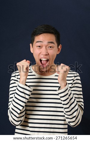Astonished young Asian man laughing and shaking two fists