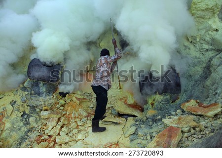 KAWAH IJEN, INDONESIA - AUGUST 9, 2011: Miner collects sulphur in the fumes of toxic volcanic gas at the sulphur mines in the crater of the active volcano of Kawah Ijen, East Java, Indonesia.