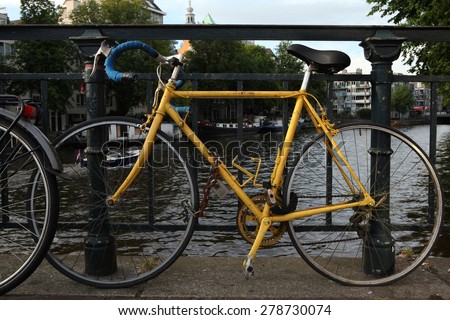 AMSTERDAM, NETHERLANDS - AUGUST 9, 2012: Old yellow bicycle parked on the bridge over a gracht in Amsterdam, Netherlands.