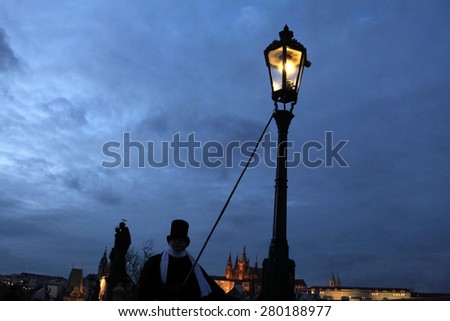 PRAGUE, CZECH REPUBLIC - DECEMBER 5, 2012: Lamplighter lights a street gas light manually during the Advent at the Charles Bridge in Prague, Czech Republic.