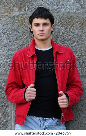 Young man in a red jacket in front of a stonewall