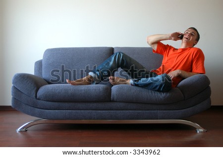 Sexy young man talking on the cell phone sitting on the sofa