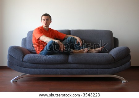 Sexy young man in an orange t-shirt sitting on the sofa