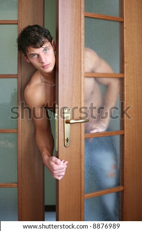 Sexy muscular man looking out the wooden door in a room