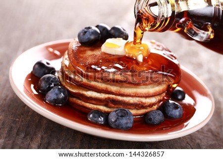 Pouring maple syrup on stack of pancakes